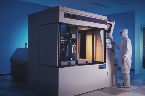 A man in a white lab coat stands beside a sophisticated machine in a laboratory setting, showcasing a professional environment.