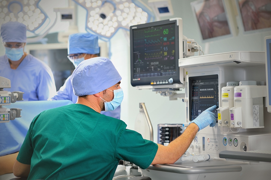 A team of doctors in scrubs collaborates at a Gas analyzer in an operation room, surrounded by medical equipment and computers
