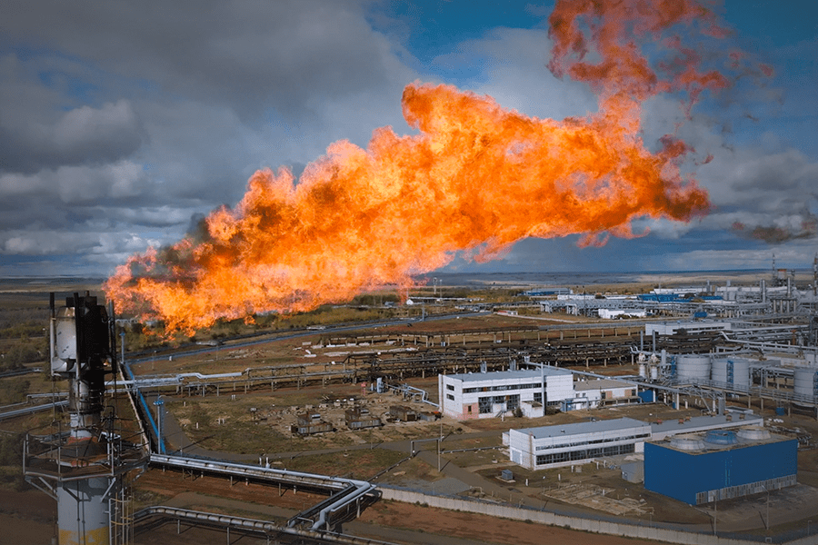 A gas flare burns brightly in the background, with the words displayed prominently in front of a factory setting.