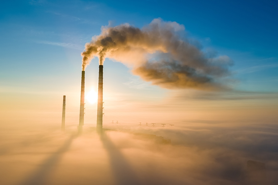 Aerial view of coal power plant high pipes with black smoke moving up polluting atmosphere at sunset.