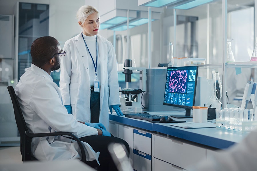 Modern Medical Research Laboratory: Two Scientists Use Computer with Screen Showing DNA Gene Analysis, Specialists Discuss Innovative Technology. Advanced Scientific Lab for Medicine, Biotechnology