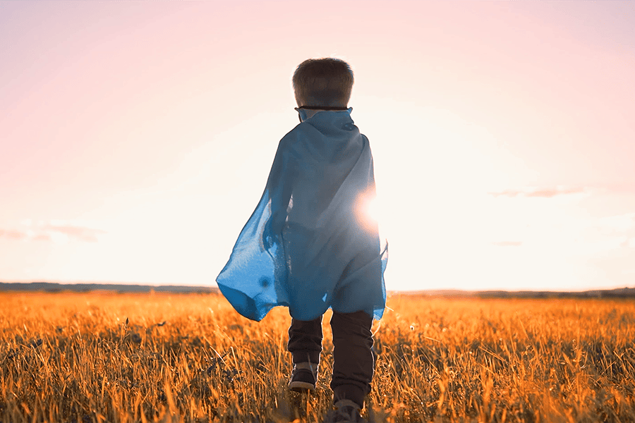 child stands in a field whilst watching the sunset