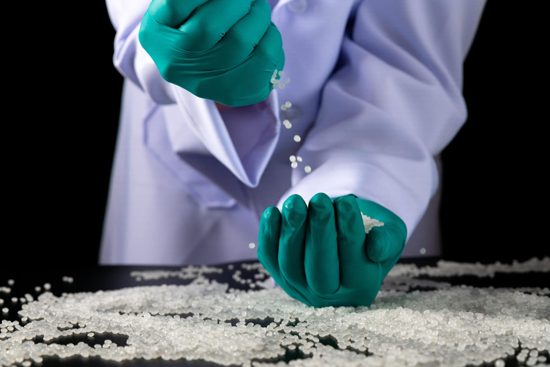 Employees wearing green gloves work with plastic beads.close-up shot of polymer pallet. Products from petrochemical plants. Scientists experiment with reducing or reusing plastic.